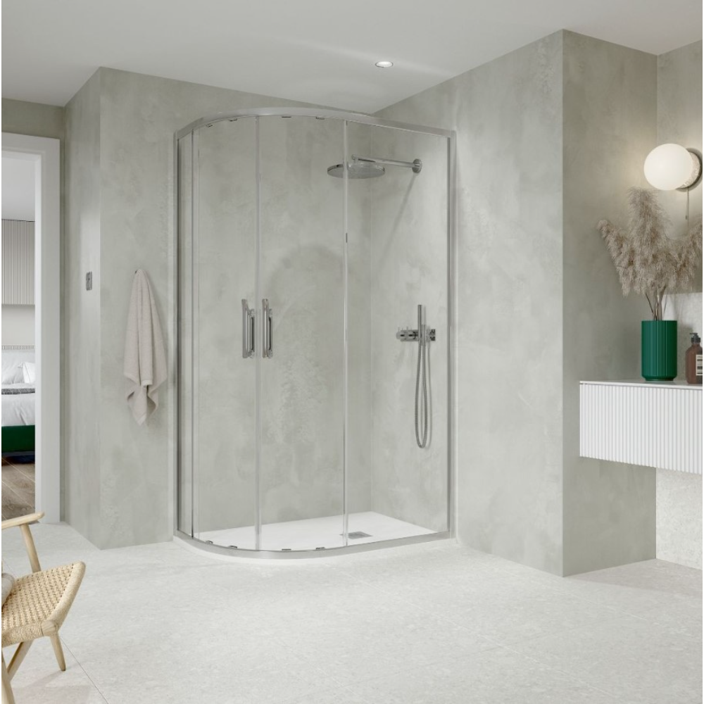 Modern chrome quadrant shower enclosure with curved glass doors in minimalist bathroom featuring light grey concrete-effect walls, white floor tiles, integrated rainfall showerhead and handheld spray, chrome fixtures, white vanity unit with green vase accent, and natural wood chair