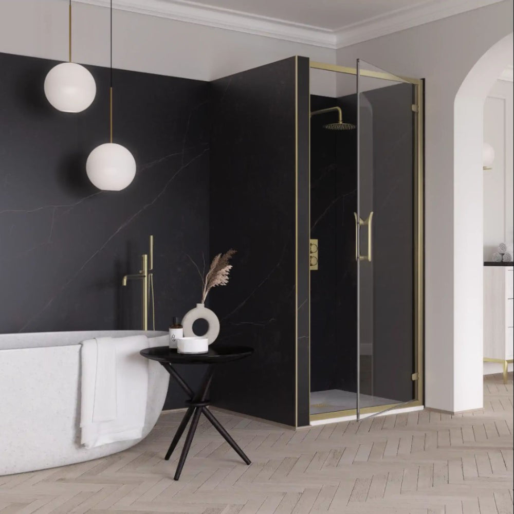 Modern bathroom featuring Flair ETO brushed brass hinge shower door with black marble-effect tiles, white freestanding bath, pendant globe lights, black side table with white ceramic vase, wooden herringbone floor and grey walls