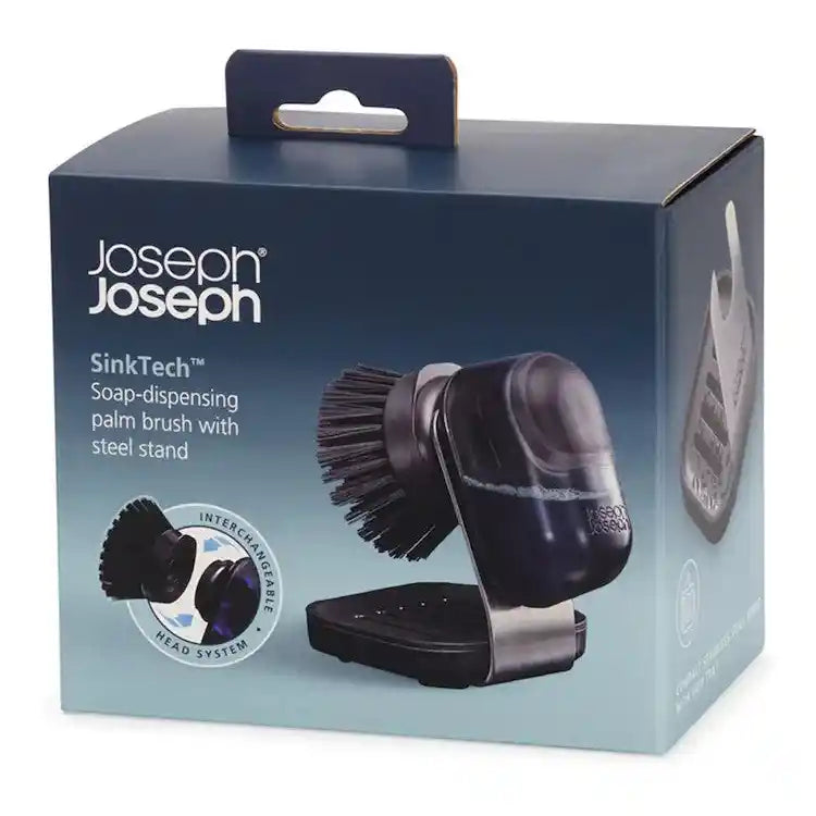 Joseph Joseph SinkTech soap-dispensing palm brush with steel stand featuring interchangeable brush heads in black and metallic gray, displayed in product packaging