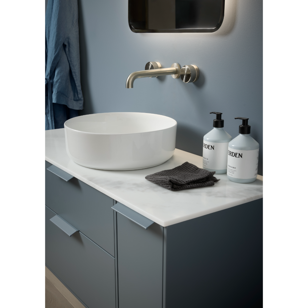 Modern bathroom vanity unit with white marble countertop, dark grey cabinetry, round white ceramic vessel sink, brass wall-mounted faucet, two pump dispensers, dark grey towel and mirror above