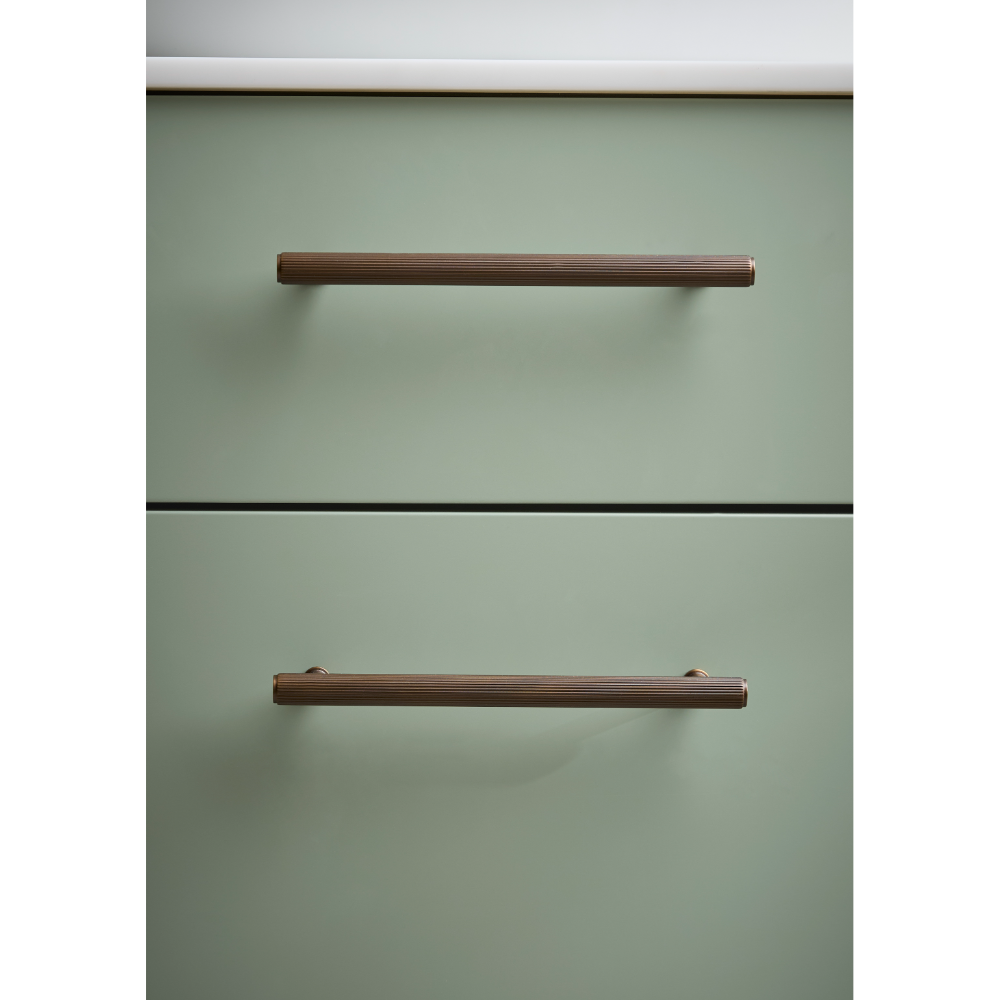 Sage green vanity unit with two horizontal bronze metal handles and black trim detail against white ceiling