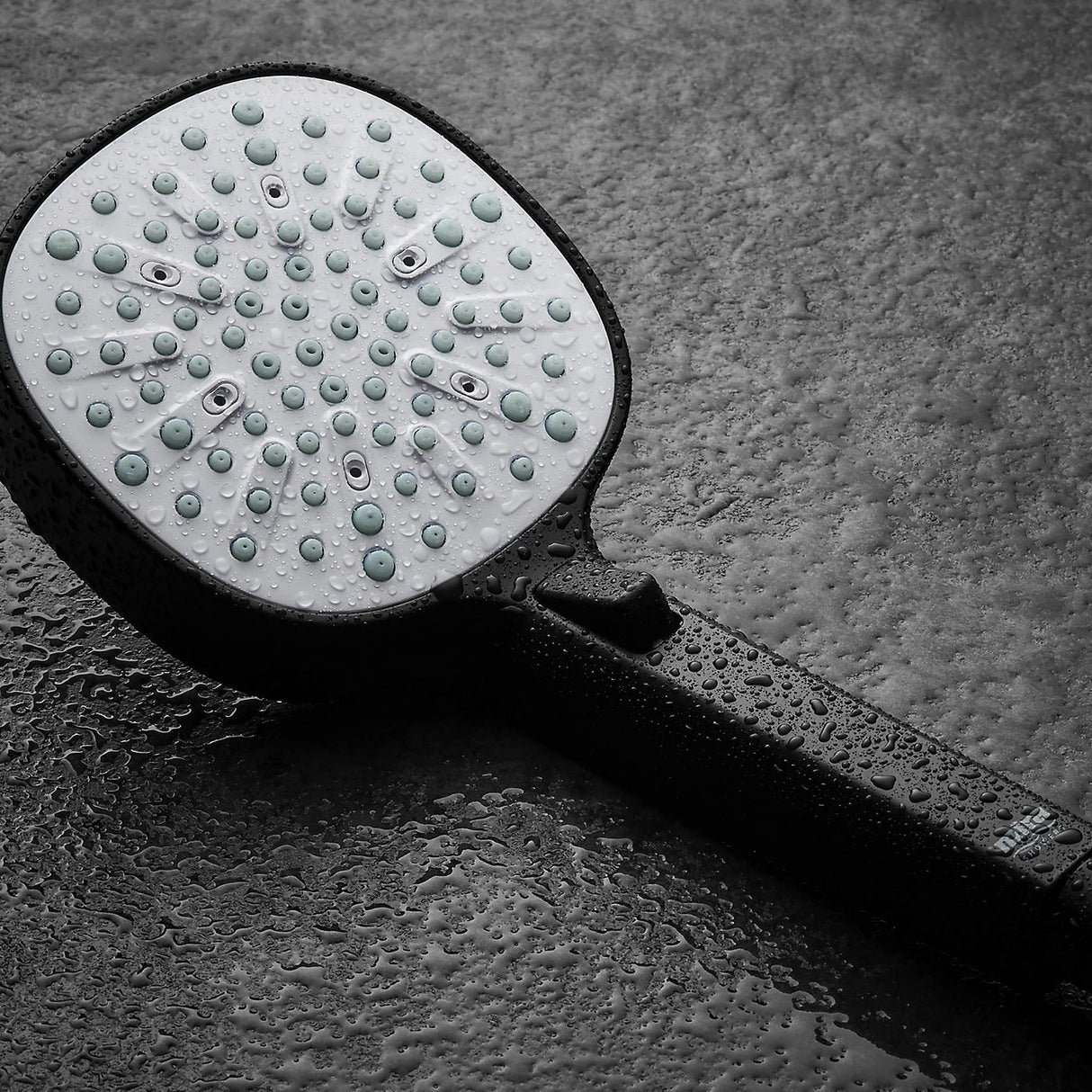 Mira Relate Dual Bar Mixer Shower in matt black finish with circular shower head showing water droplets on wet surface against grey textured background