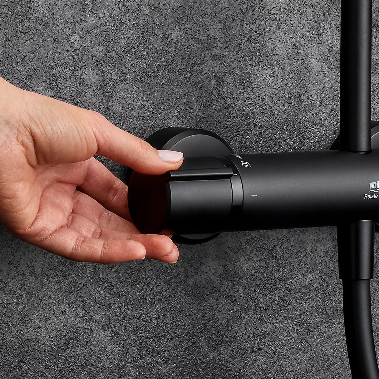 Hand demonstrating the rotating dual bar control of a Mira Relate matt black mixer shower valve mounted on a textured grey bathroom wall