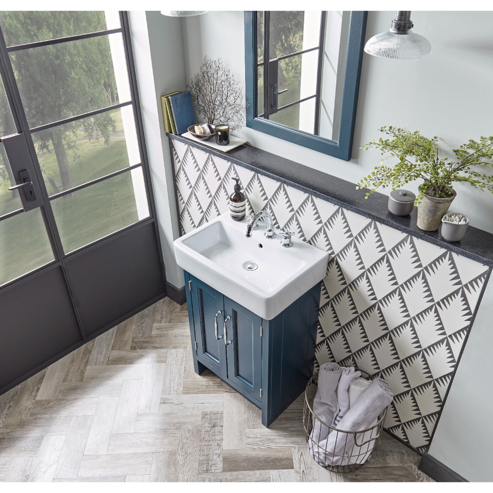Roper Rhodes Hampton vanity unit in slate grey with white rectangular sink, black countertop and geometric patterned backsplash tile, positioned in modern bathroom with herringbone wood-effect flooring, large windows, and decorative accessories