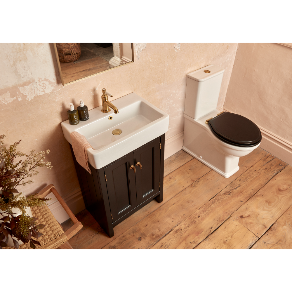 Modern bathroom vanity unit in Matt Black with white rectangular ceramic sink, brass tap, and black toilet seat, set on wooden flooring with pink walls and dried floral decoration