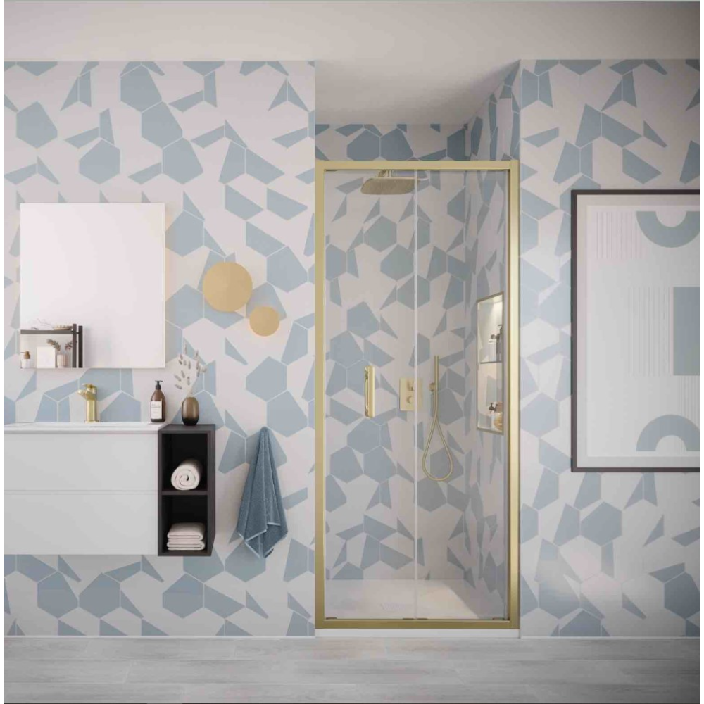 Modern bathroom with Flair ILI brushed brass bifold shower door featuring geometric patterned blue and white tiles, white vanity with black storage unit, framed mirrors, and gold pendant lights above the shower enclosure