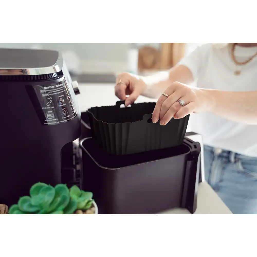 Woman in white shirt removing black silicone air fryer liner from air fryer basket, showing product functionality and size