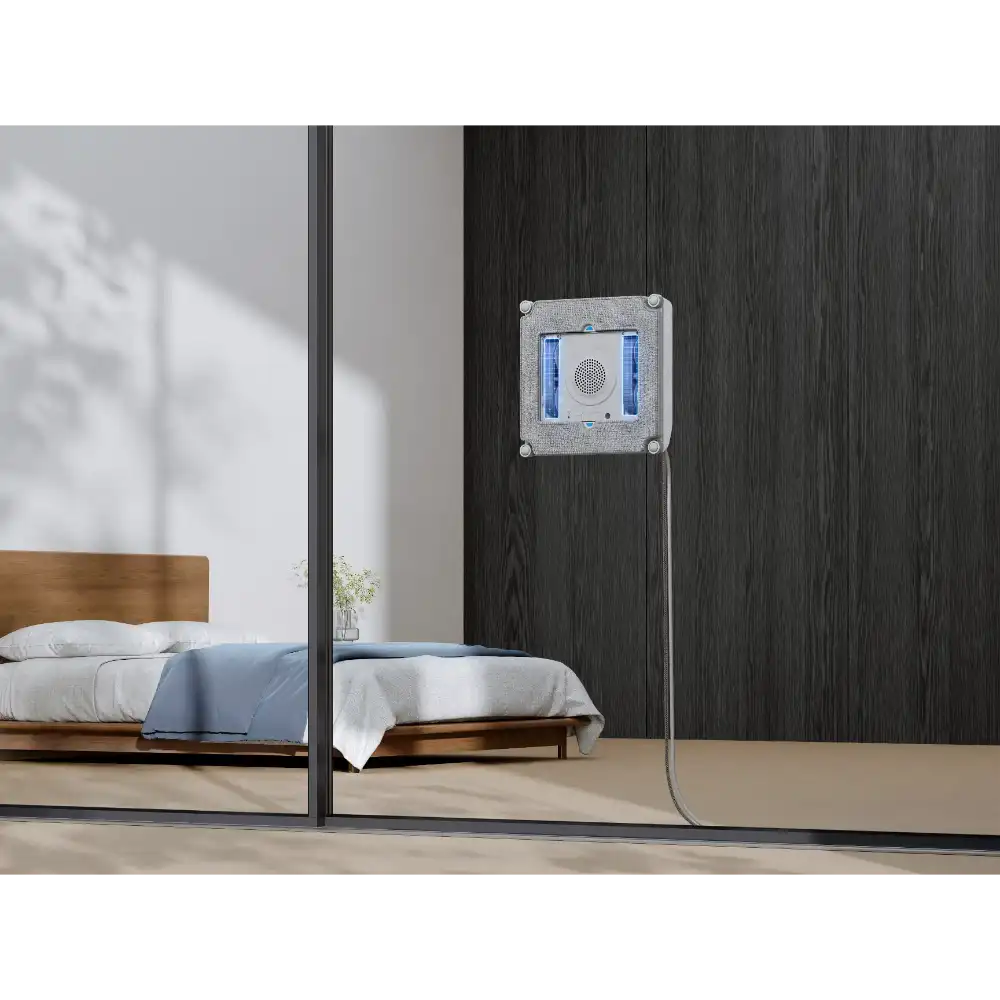 Ecovacs Winbot Mini beige robot window vacuum mounted on dark wood wall next to bedroom with wooden bed and mirror reflection