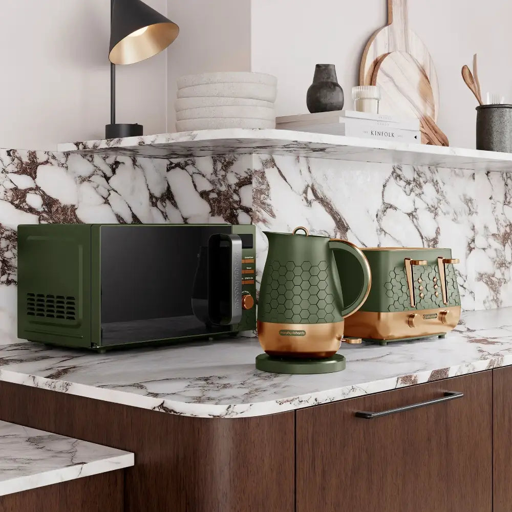 Morphy Richards Cassini olivine green microwave displayed on a marble countertop alongside matching green kettle and toaster, modern kitchen setting with wooden cabinetry and decorative accessories