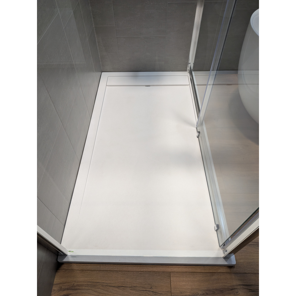 White rectangular shower tray with chrome frame and glass panel in modern bathroom with grey tile walls and wooden flooring