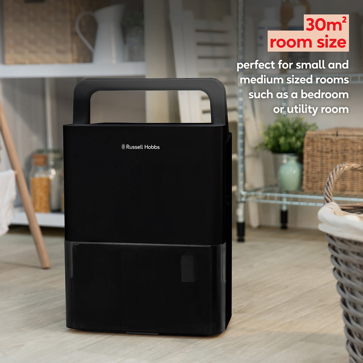Russell Hobbs black portable dehumidifier with carry handle displayed in a modern kitchen setting, 30m² room capacity specification highlighted for bedrooms and utility rooms
