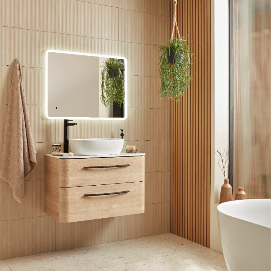 Modern bathroom vanity unit in light wood with white ceramic basin, black faucet, illuminated mirror, wall-mounted wooden drawers, and natural textured wall tiles in warm neutral tones