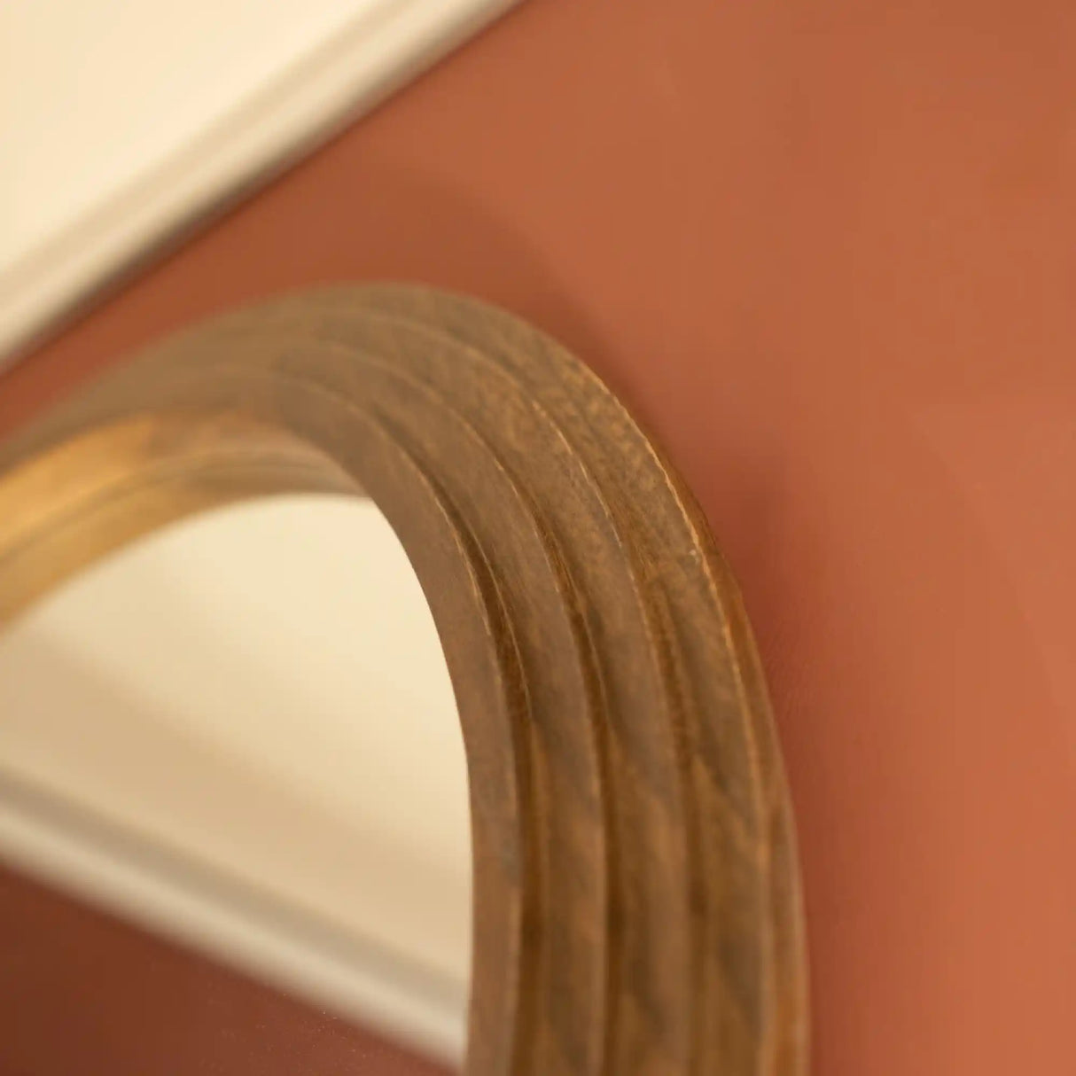 Close-up detail of natural wood frame on Tara Lane stepped arched wall mirror showing warm honey-toned wooden trim against terracotta wall background