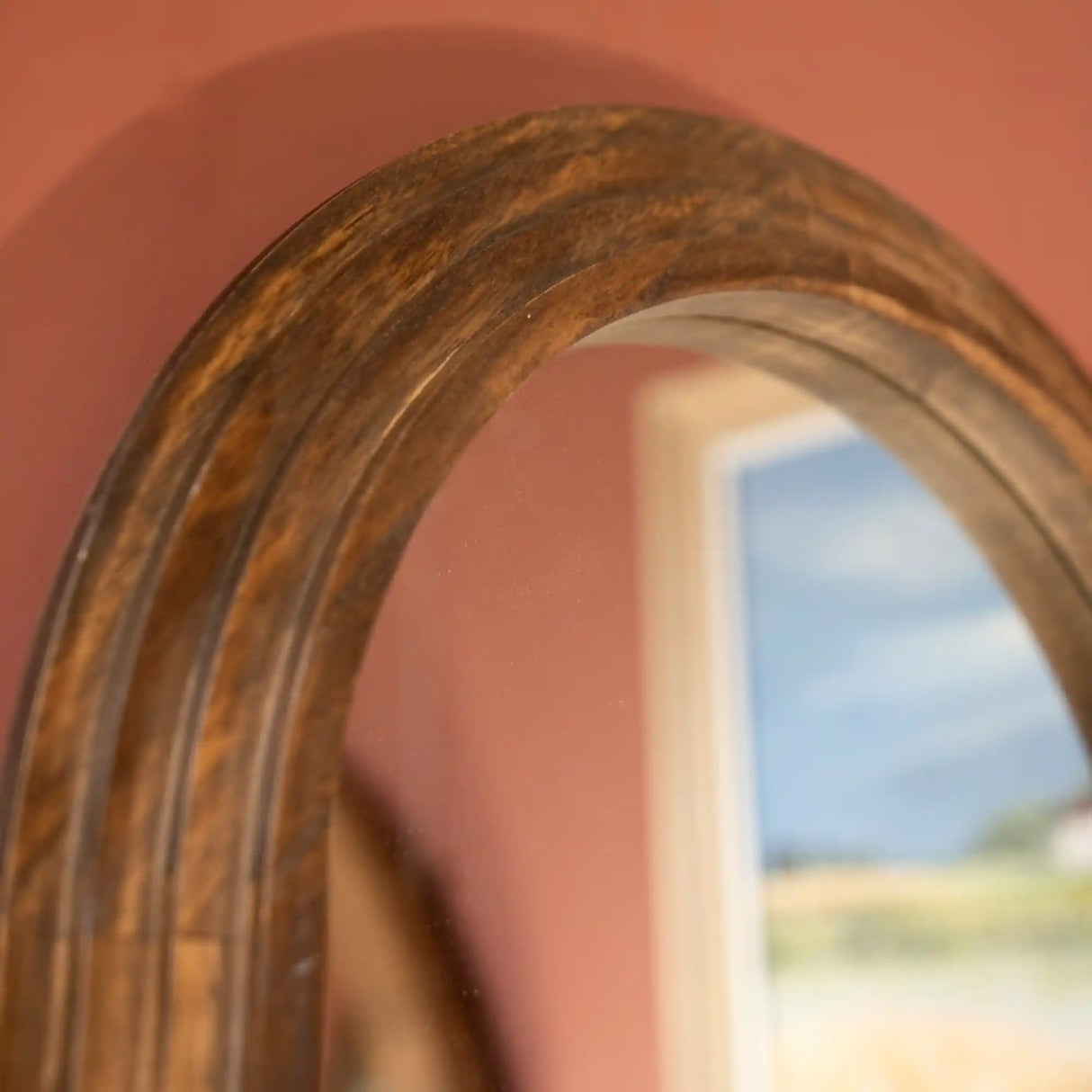 Wooden framed pill-shaped mirror with natural wood grain finish reflecting pink wall and blue sky, Tara Lane dressing mirror 45cm x 150cm
