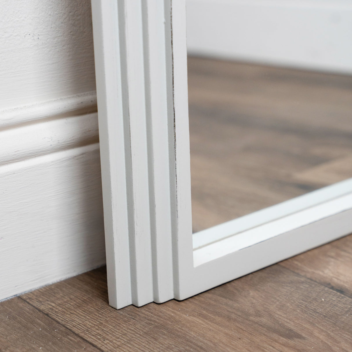 White framed leaning mirror with arched top displayed against wooden flooring and white wall