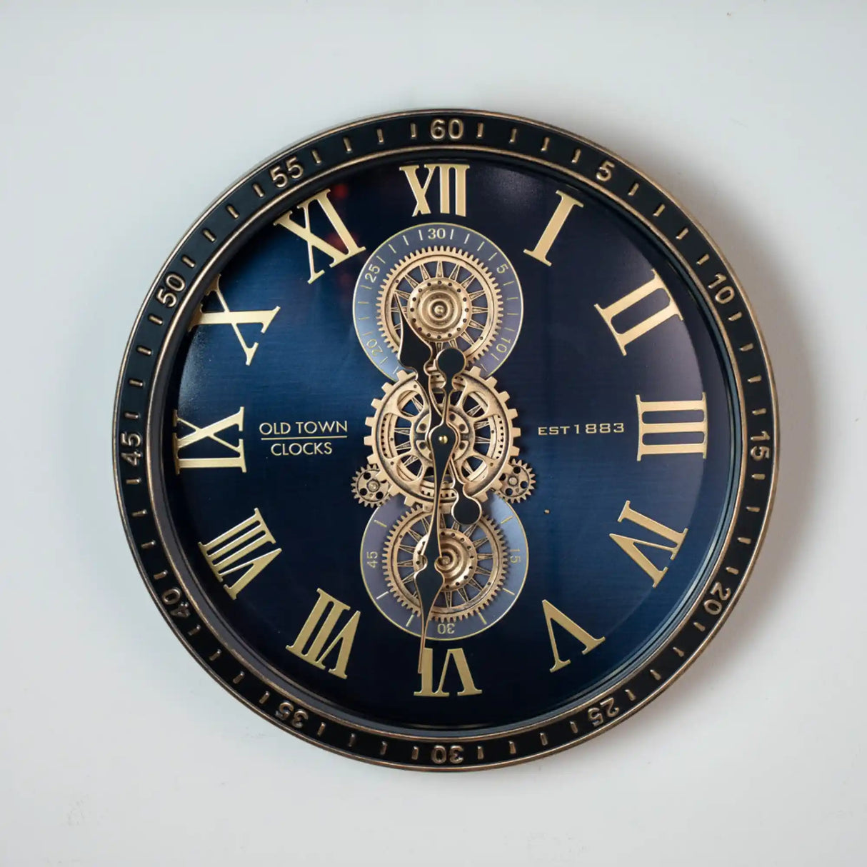 Large decorative wall clock by Tara Lane Old Town Clocks, 50cm diameter, featuring a black face with gold Roman numerals, exposed brass gear mechanism in the center, established 1883, minute markers around the outer edge, steampunk style design