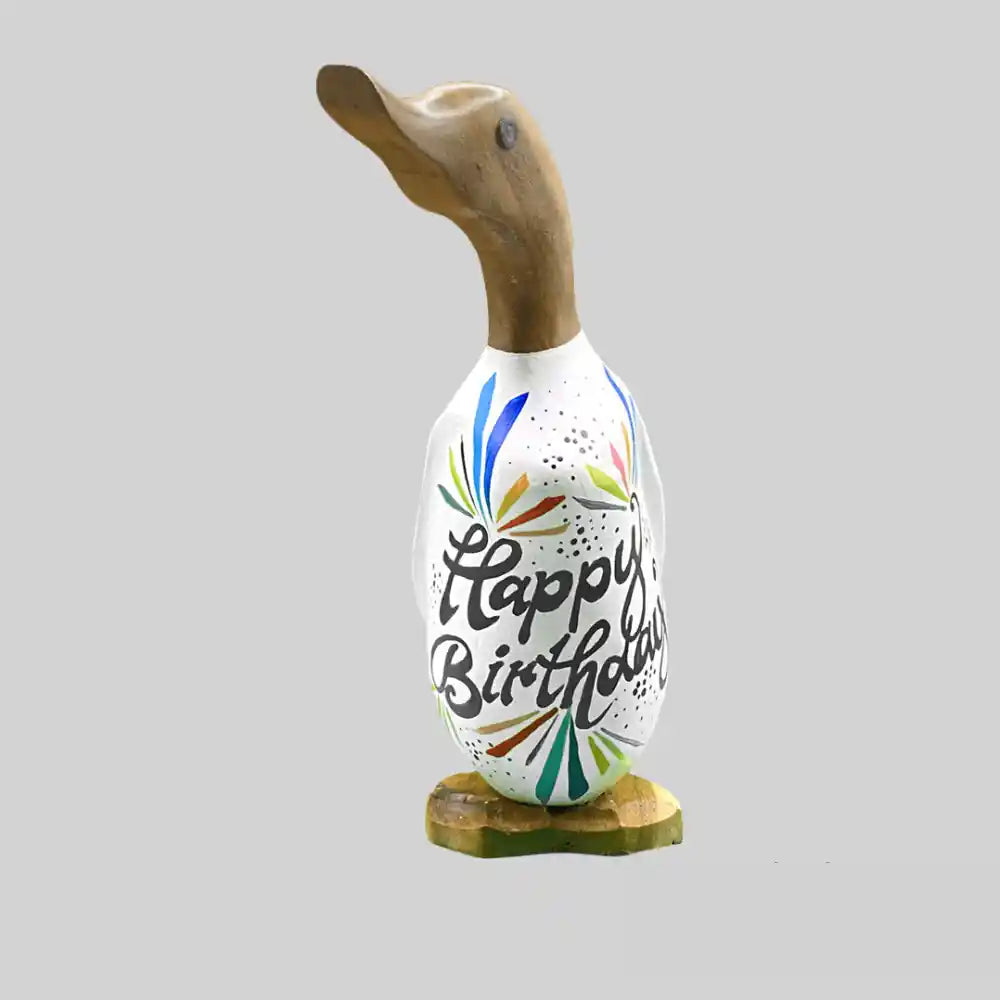 Wooden duck figurine with carved head and neck in natural wood, featuring a white ceramic body decorated with colorful hand-painted "Happy Birthday" text and festive burst designs in blue, green, pink and gold, mounted on a wooden base