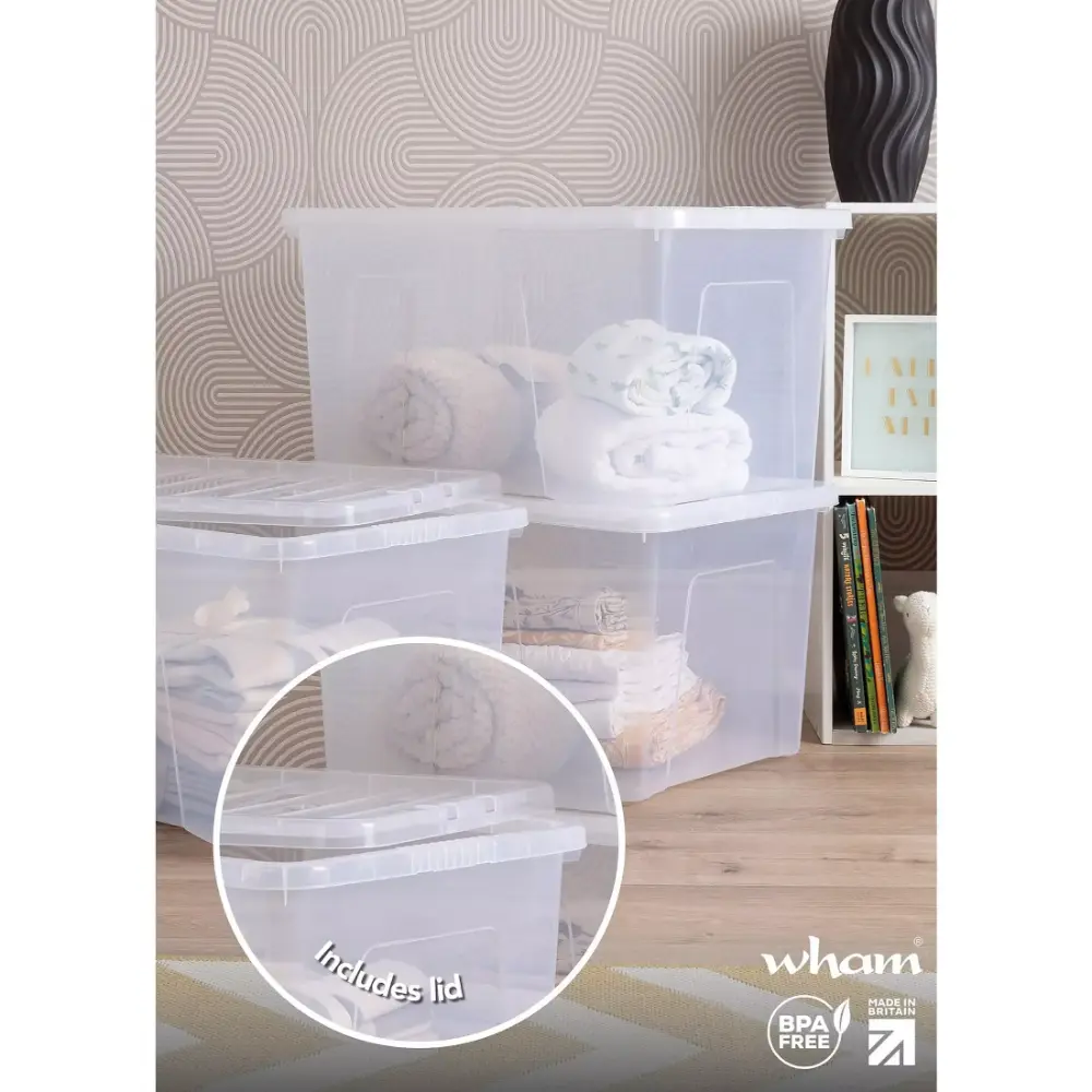 Wham 60 litre clear plastic storage box with lid displayed in a bedroom setting containing folded white bedding and textiles, featuring a geometric patterned wallpaper background and wooden flooring, with detail circle highlighting the included lid, BPA free and made in Britain