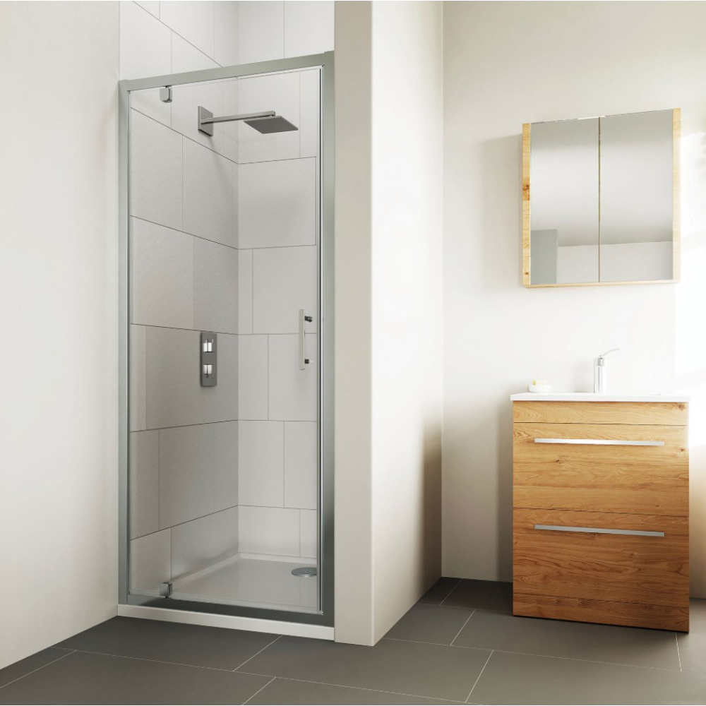 Modern chrome pivot shower door with clear glass panel installed in minimalist bathroom with white subway tiles, grey floor tiles, wooden vanity cabinet and mirror cabinet