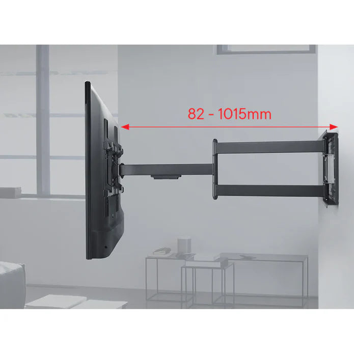 Black full motion TV wall bracket mount with articulating arm extended showing 82-1015mm extension range, mounted on white wall with grey structural elements in background