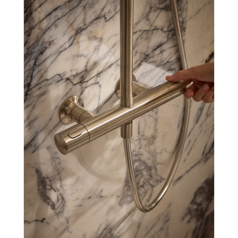Close-up of a modern brushed nickel shower system with cylindrical bar rail mounted on marble tile wall, showing hand adjusting the rail fixture against veined white and grey marble background
