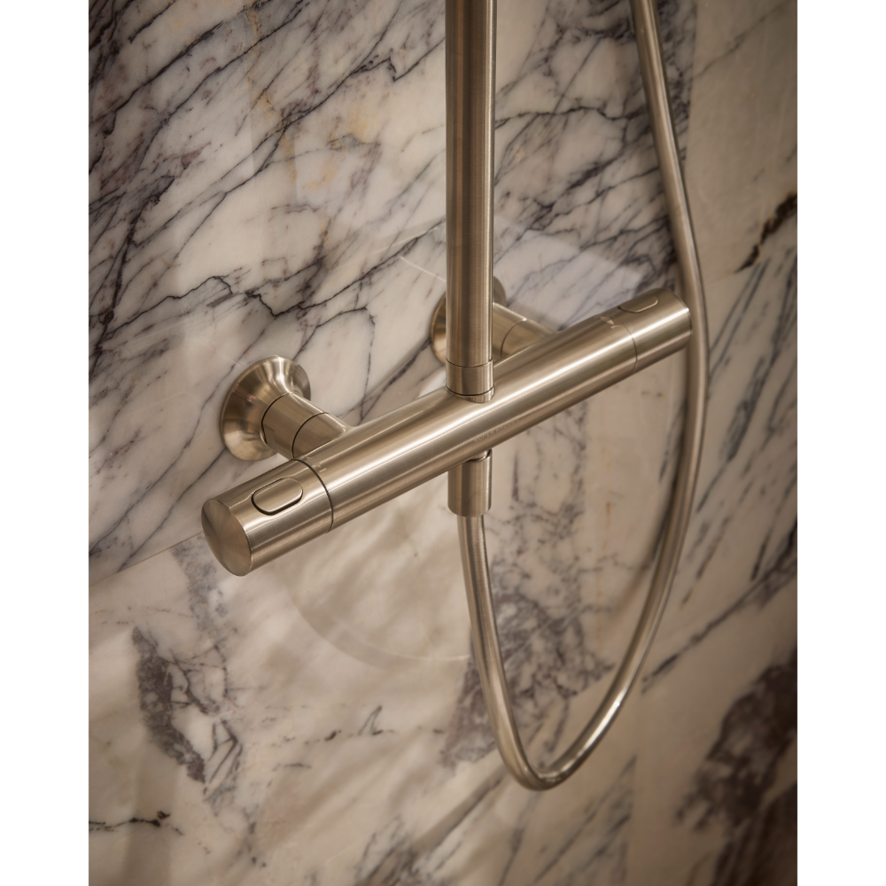Close-up of Roper Rhodes Walcot concealed shower system in brushed nickel finish mounted on marble wall with horizontal bar and vertical rail against veined white and grey marble tiles