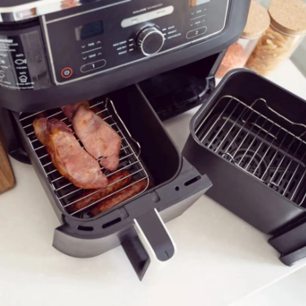 Two black wire shelf inserts for air fryers displayed with cooked bacon on the left basket, shown alongside an air fryer unit with digital controls on a white surface