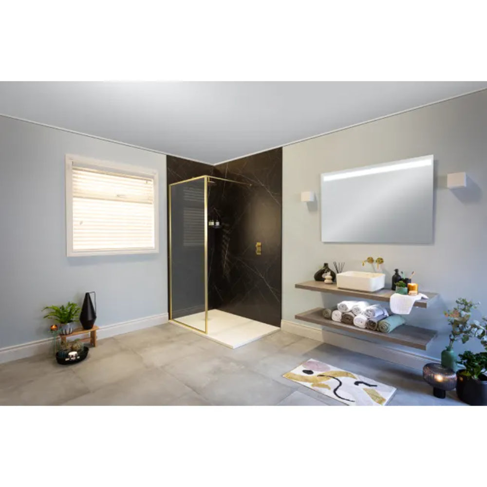 Modern bathroom featuring Merlyn 6 Series Sleek wetroom panel with brushed brass frame and black marble effect panels, cream tile flooring, floating wooden shelves with white vessel sink, illuminated mirror, and contemporary fixtures