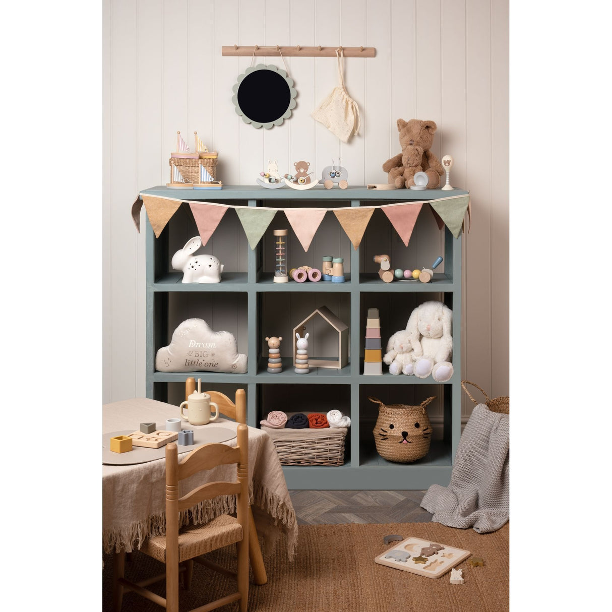 Bambino wooden music set displayed in a grey cubby shelf unit in a neutral nursery room with natural wood furniture, soft toys, and pastel decorative elements