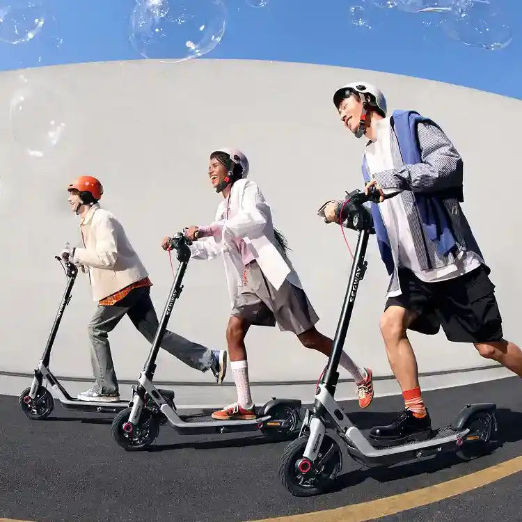 Three people riding black electric scooters against a white curved wall with blue sky, wearing helmets and casual athletic clothing in bright sunlight