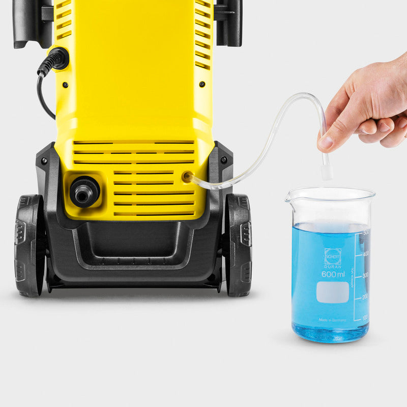 Yellow and black Karcher K3 pressure washer with blue cleaning solution in measuring beaker, demonstrating water and detergent mixing for the eco-friendly power washer
