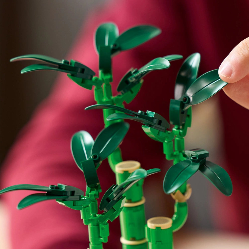 LEGO Lucky Bamboo set 10344 featuring articulated green plastic bamboo stalks with poseable leaves and tan bamboo segment connectors, displayed against a pink blurred background with a hand positioning one of the leaf elements