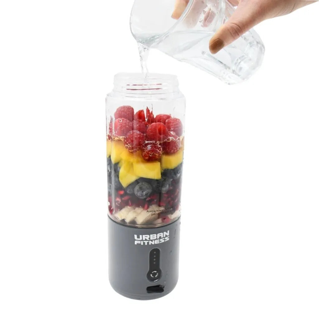 Urban Fitness VitalFuse portable blender in grey with layered fruits including raspberries, mango, and blueberries, water being poured into the blender jar from above