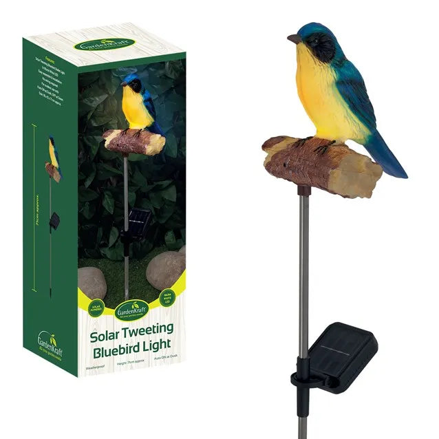 Gardenkraft Solar Tweeting Bluebird Light showing product packaging on left and assembled garden stake light on right featuring a blue and yellow bird figurine perched on a brown textured branch with black solar panel base