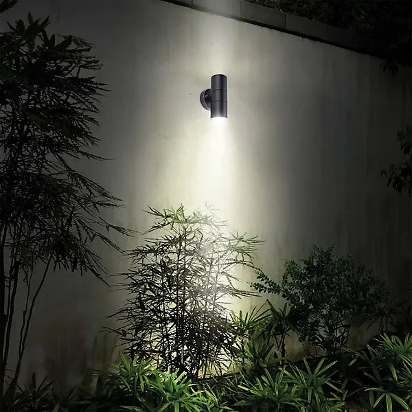 Luceco Azurar black stainless steel up down external wall light mounted on white wall illuminating green foliage and plants below