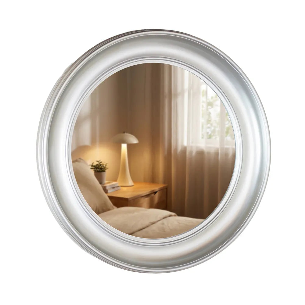 Round champagne-framed mirror reflecting a bedroom with wooden nightstand, table lamp, potted plant and curtains, 90cm Tara Lane Lyla design