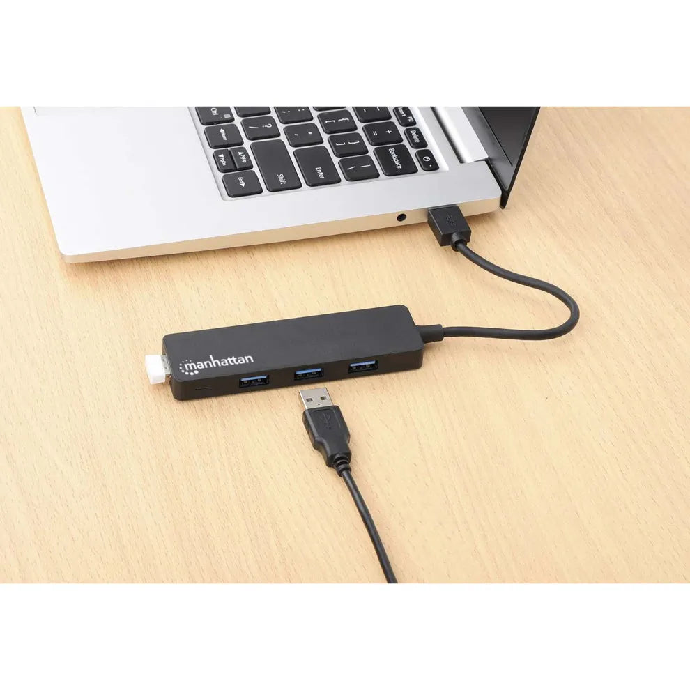 Manhattan 4 Port USB 3.0 powered hub in black connected to MacBook laptop on wooden desk with USB cable and connector visible