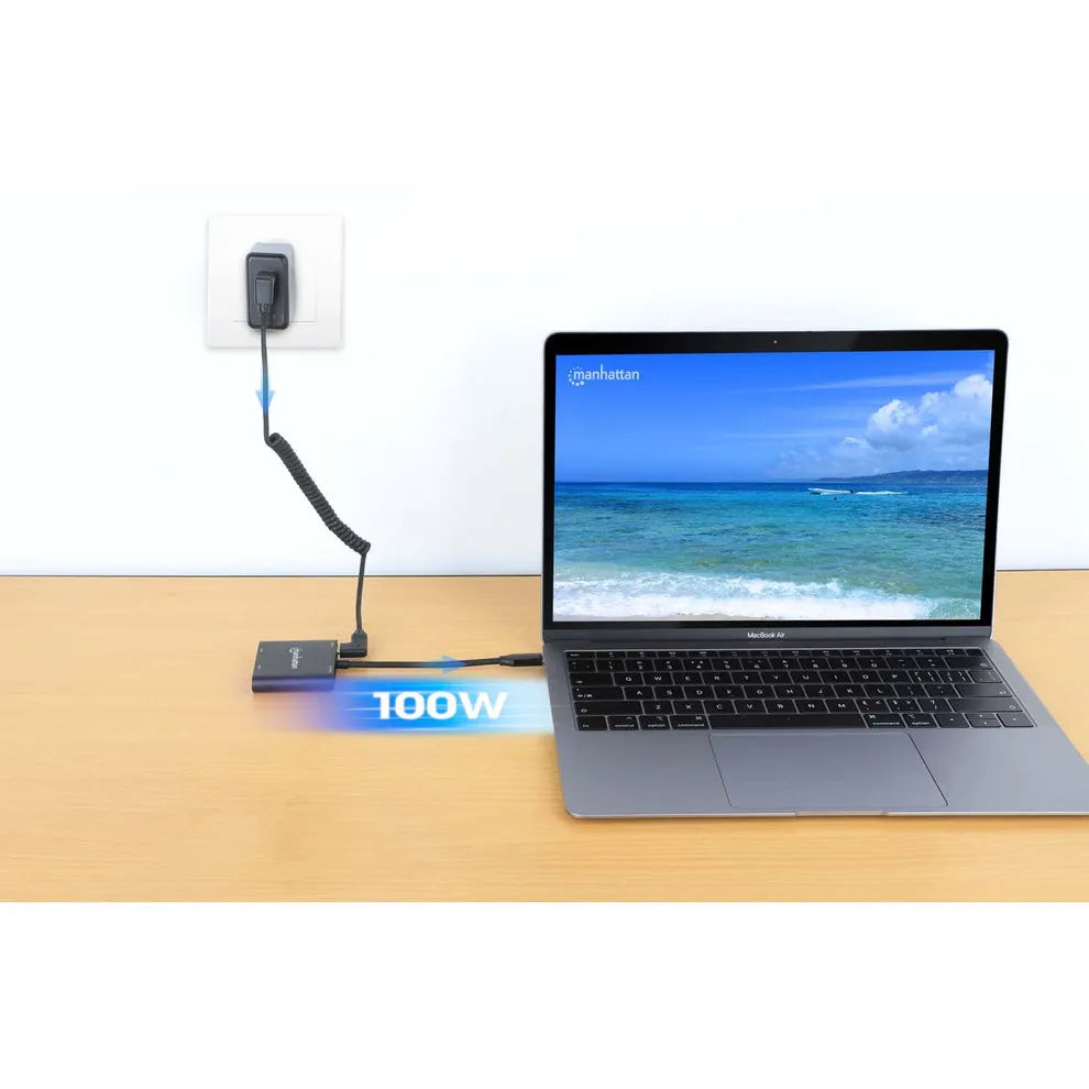 Manhattan USB-C multiport adapter displaying 100W power delivery connected to MacBook Air via coiled cable, with wall power adapter and HDMI connection shown in home office setup