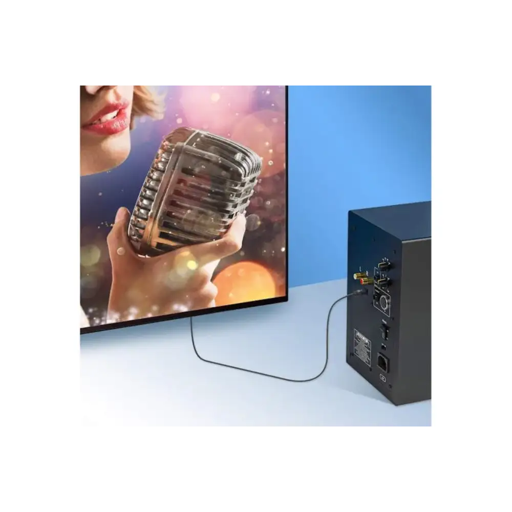 Black Manhattan Toslink digital optical audio cable connected between a black audio amplifier box and a flat screen monitor displaying a woman holding a vintage microphone against a colorful gradient background
