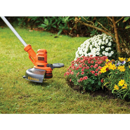 Black and Decker BESTA530 orange corded grass strimmer in use on lawn next to flower bed with white, red and yellow flowers