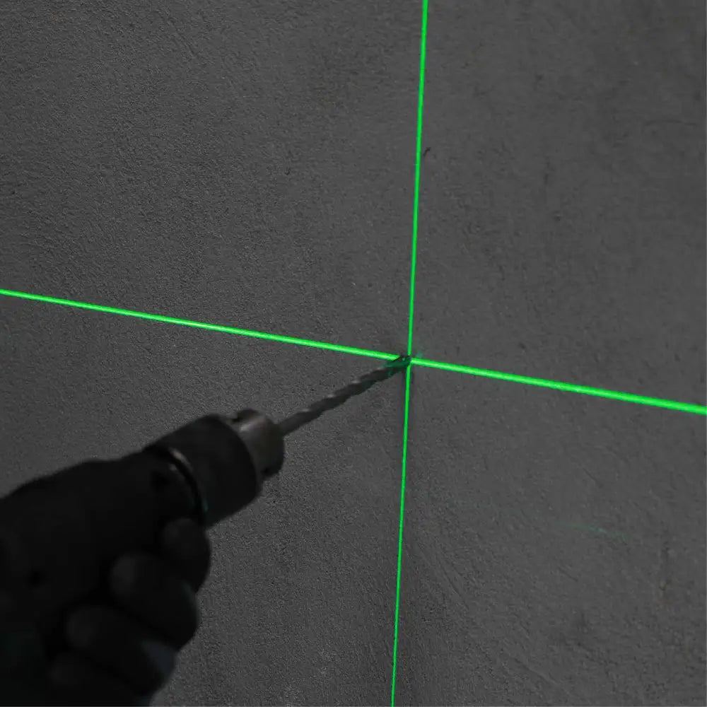 Green laser level tool projecting crosshair lines on dark concrete wall surface with black handle visible in foreground