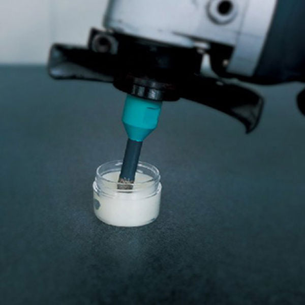 Diamond brazed tile drill bit 12mm M14 mounted on drilling machine with turquoise cooling liquid dispensing into white ceramic test sample