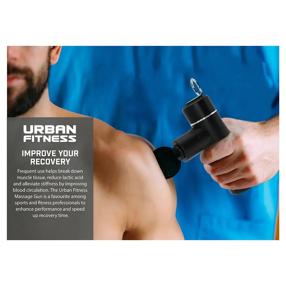 Man in blue shirt holding black Urban Fitness mini massage gun against bare shoulder, demonstrating muscle recovery and massage therapy on white background