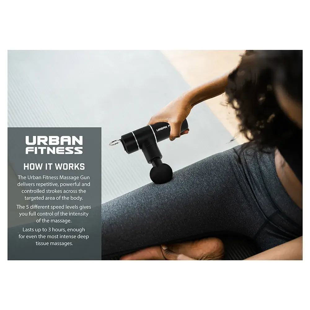 Person using black Urban Fitness mini massage gun on arm muscle with grey compression sleeve against sky background, demonstrating deep tissue massage technique with product information panel on left