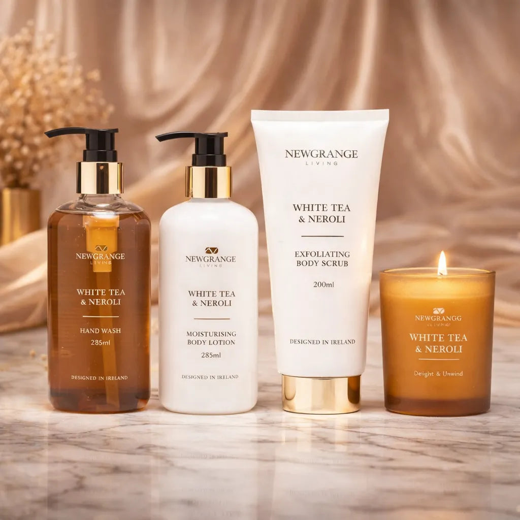 Newgrange Living White Tea and Neroli four-piece body care set featuring a brown glass hand wash bottle, white moisturising body lotion, white exfoliating body scrub, and amber glass scented candle arranged on a marble surface with a beige fabric backdrop