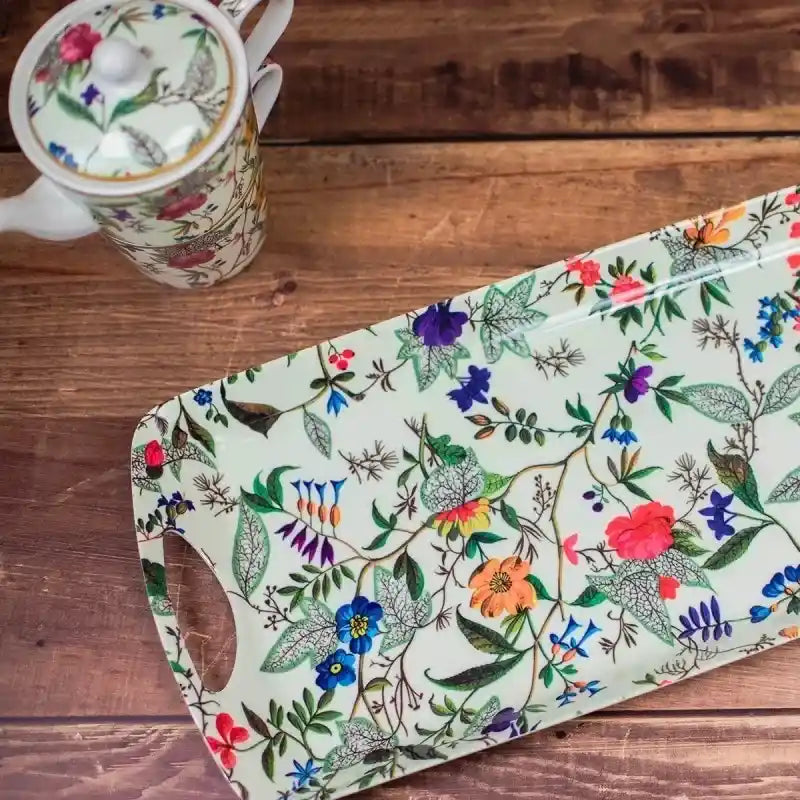 William Kilburn Medium Serving Tray with Handles featuring colorful floral botanical print on cream background, displayed on wooden surface next to matching porcelain mug with pink and purple flowers