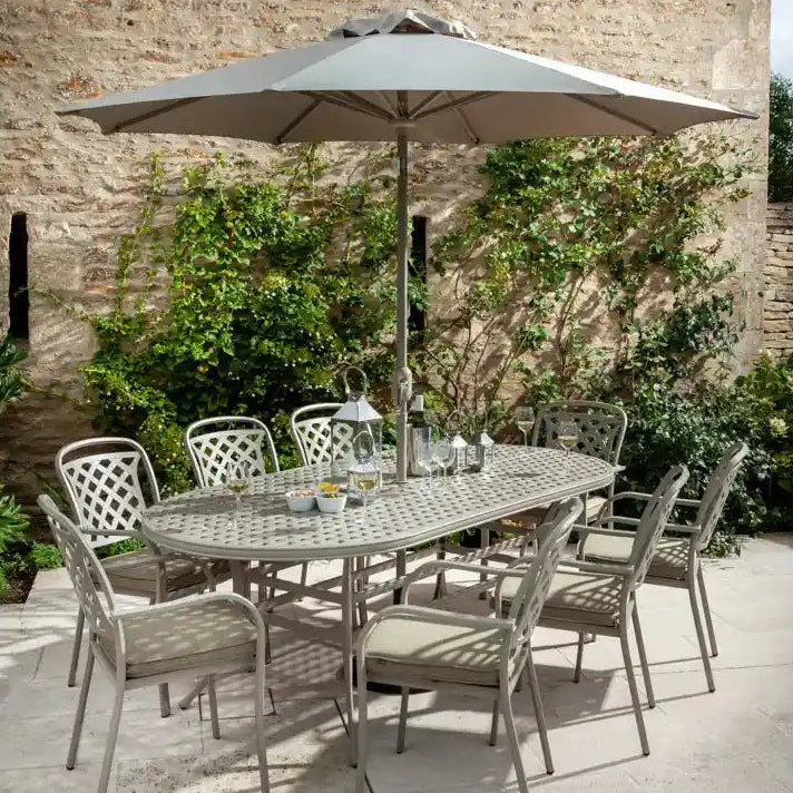 Hartman Berkeley 8 seater cast aluminium oval garden furniture set in taupe with grey cushions, featuring 6 patterned chairs and 2 armchairs around an oval table with integrated umbrella hole, complete with grey parasol, set on a stone patio against a brick wall with climbing ivy