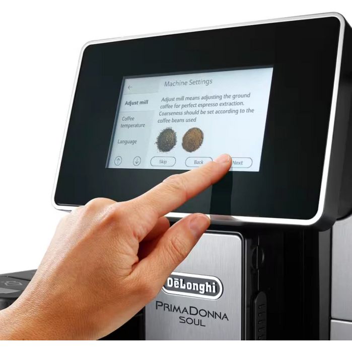 Hand touching touchscreen display of DeLonghi PrimaDonna Soul automatic coffee machine in brushed metal black finish, showing Machine Settings menu with grind adjustment options and coffee bean texture samples