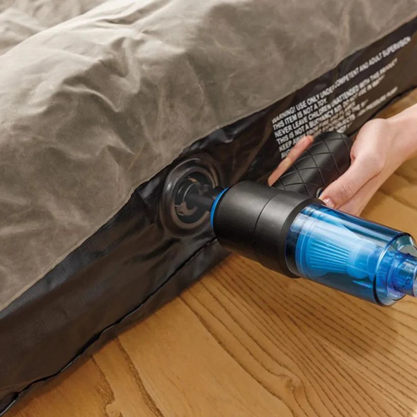 Person holding JML Go Vac portable handheld vacuum cleaner with blue water tank attachment over wooden floor next to bed with grey bedding