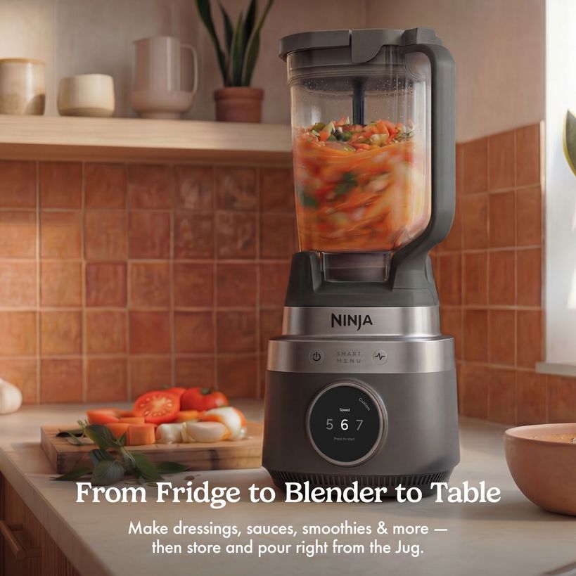 Ninja CrushBOSS 1200W intelligent blender in black and stainless steel on a kitchen counter blending chopped tomatoes and vegetables, with fresh produce on a wooden cutting board nearby and warm terracotta tile backsplash, alongside the text From Fridge to Blender to Table